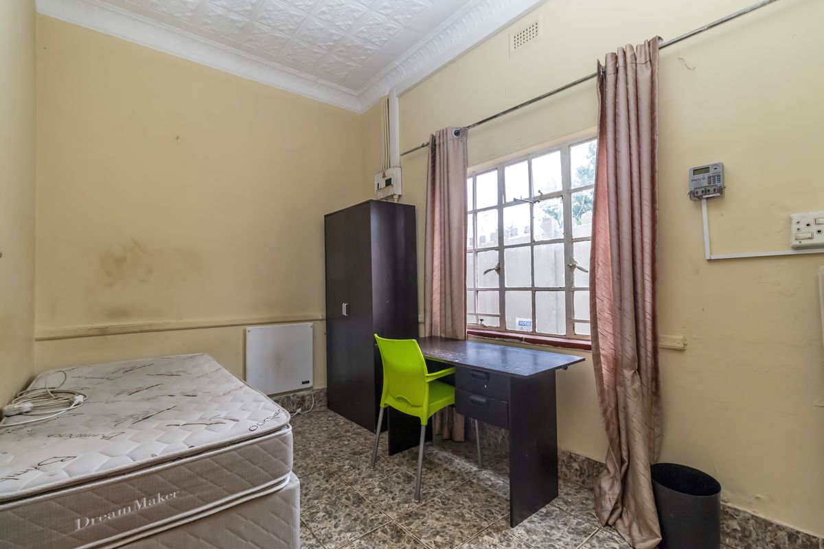 A bedroom featuring tiled flooring, a pressed metal ceiling, and a steel-framed window, requiring cosmetic updates to the wall finishes.