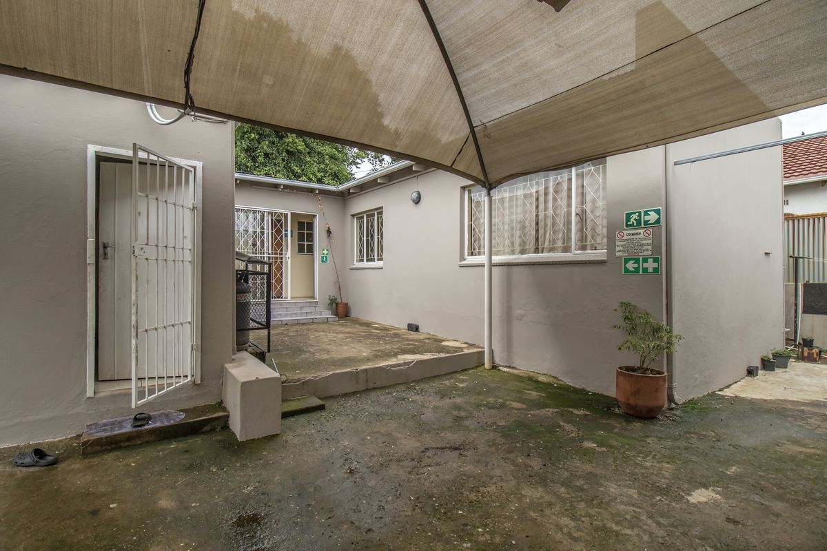 Rear exterior area featuring a concrete patio covered by a shade sail, with security gates and bars installed on the building access points.