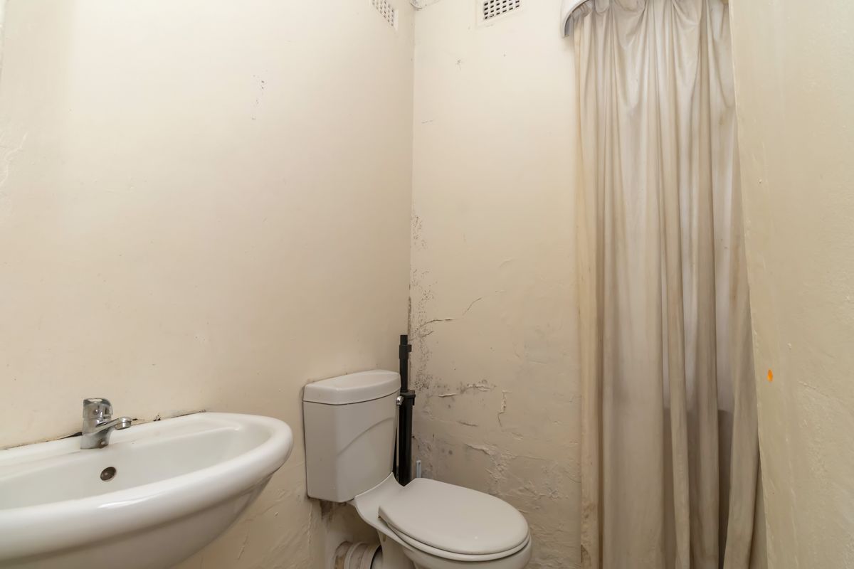 A small bathroom featuring a pedestal basin and toilet, currently requiring significant cosmetic repairs and wall surface restoration.