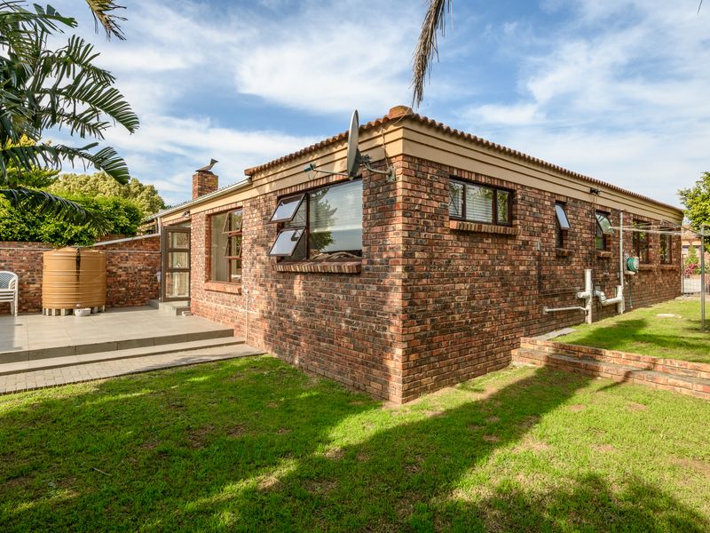 Rear view of a face brick townhouse featuring a paved patio area, a water tank, and a private garden space.