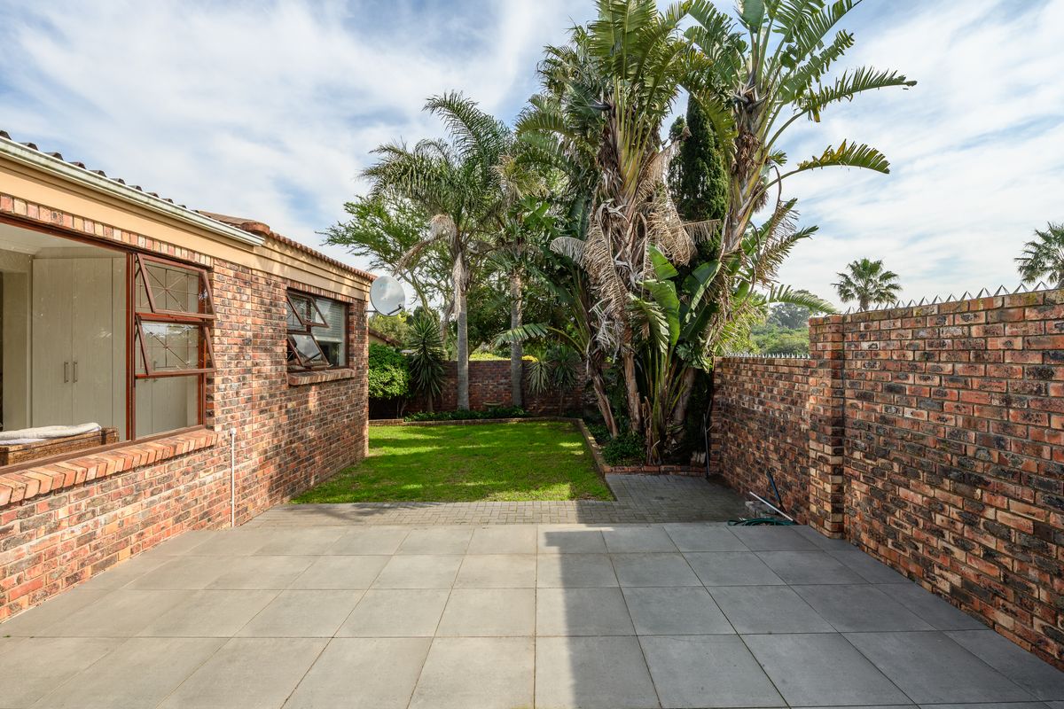 A private rear garden featuring a paved patio area, established landscaping, and secure brick boundary walls.