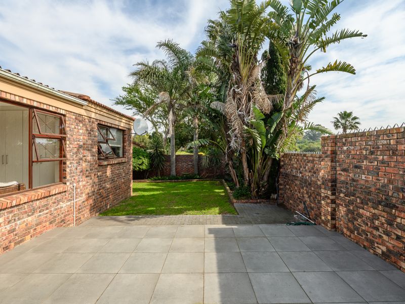 A private rear garden featuring a paved patio area, established landscaping, and secure brick boundary walls.