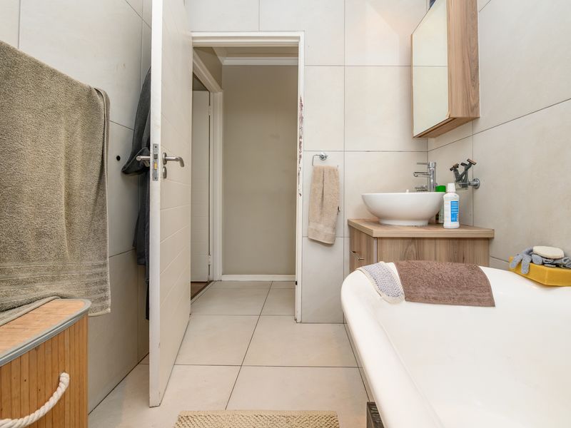A modern bathroom featuring a freestanding bathtub, a vessel sink set on a wooden vanity, and neutral wall tiling.
