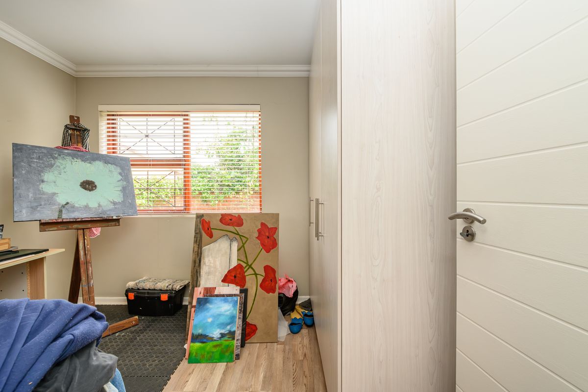 A bedroom featuring light wood-grain built-in cupboards, laminate flooring, and a window fitted with security bars and venetian blinds.