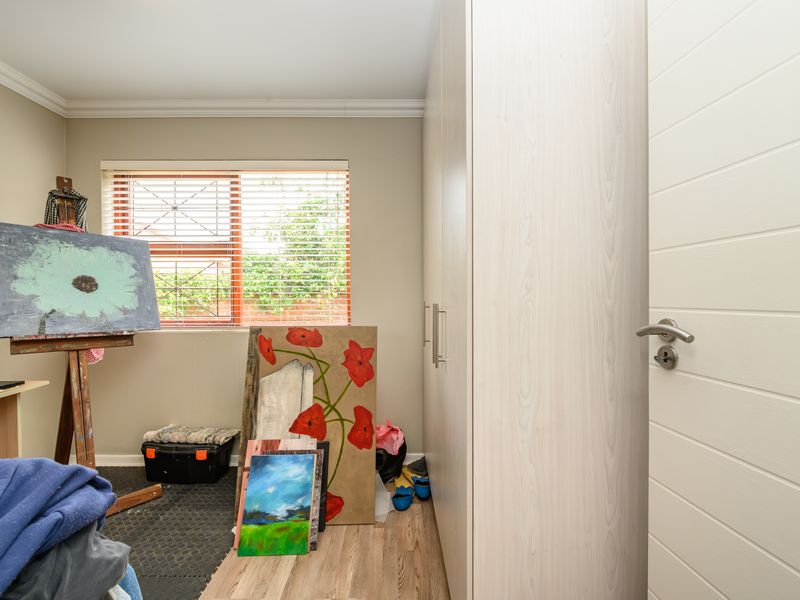 A bedroom featuring light wood-grain built-in cupboards, laminate flooring, and a window fitted with security bars and venetian blinds.