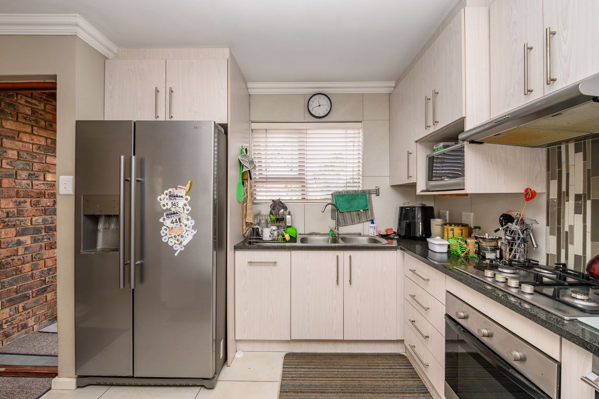 A functional kitchen featuring light wood-finish cabinetry, granite countertops, a gas hob, built-in oven, and an exposed brick feature wall.