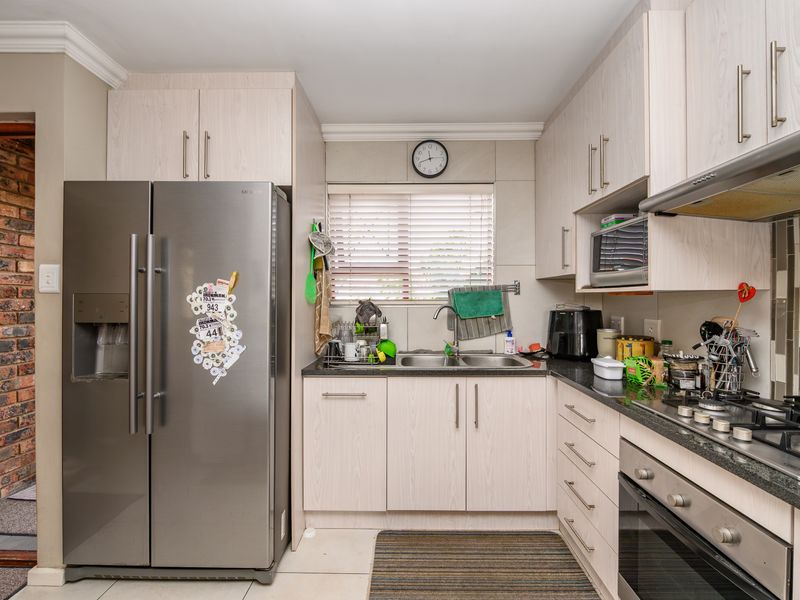A functional kitchen featuring light wood-finish cabinetry, granite countertops, a gas hob, built-in oven, and an exposed brick feature wall.