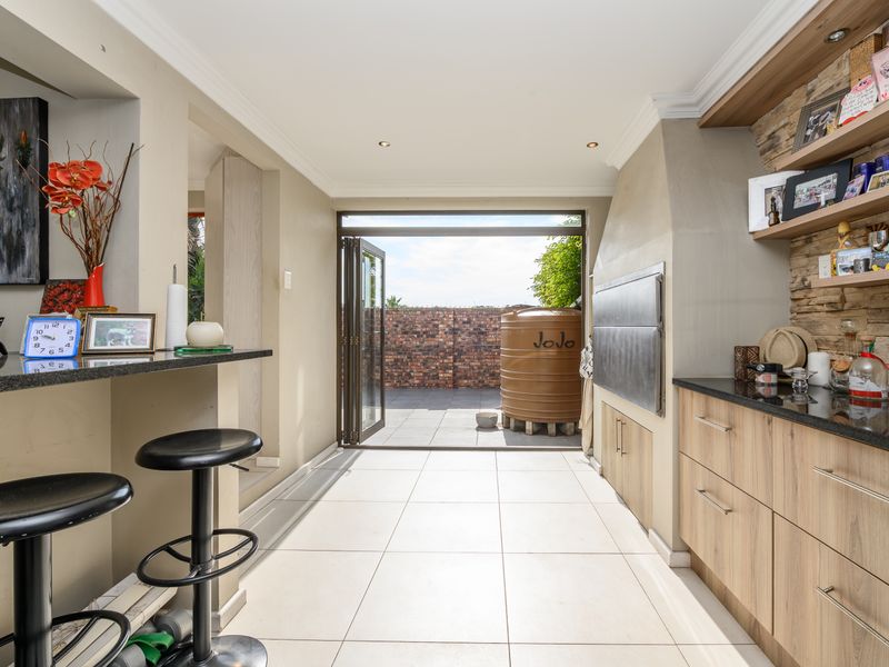 Covered patio area featuring a built-in braai, stone-clad feature wall, granite countertops, and bi-fold doors opening to the rear garden.