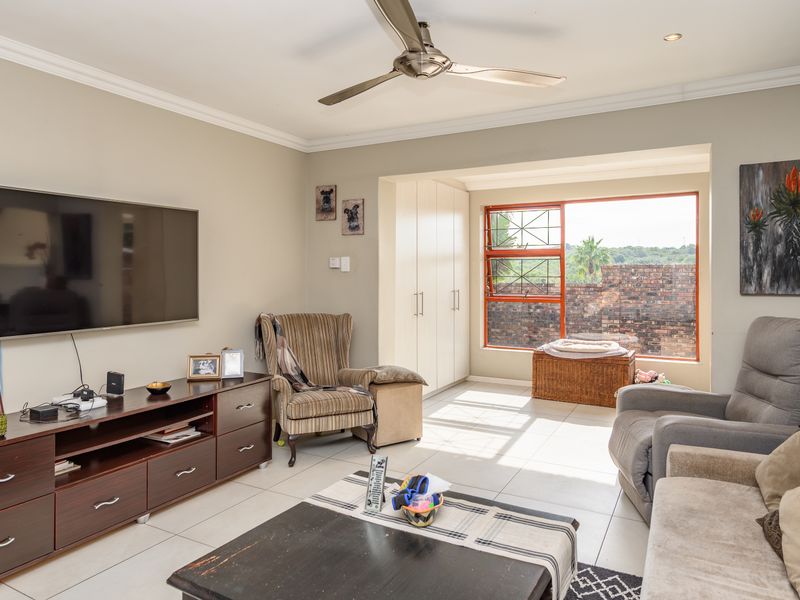 A bright living room featuring tiled flooring, a ceiling fan, recessed lighting, and built-in storage cupboards with natural light from the window.