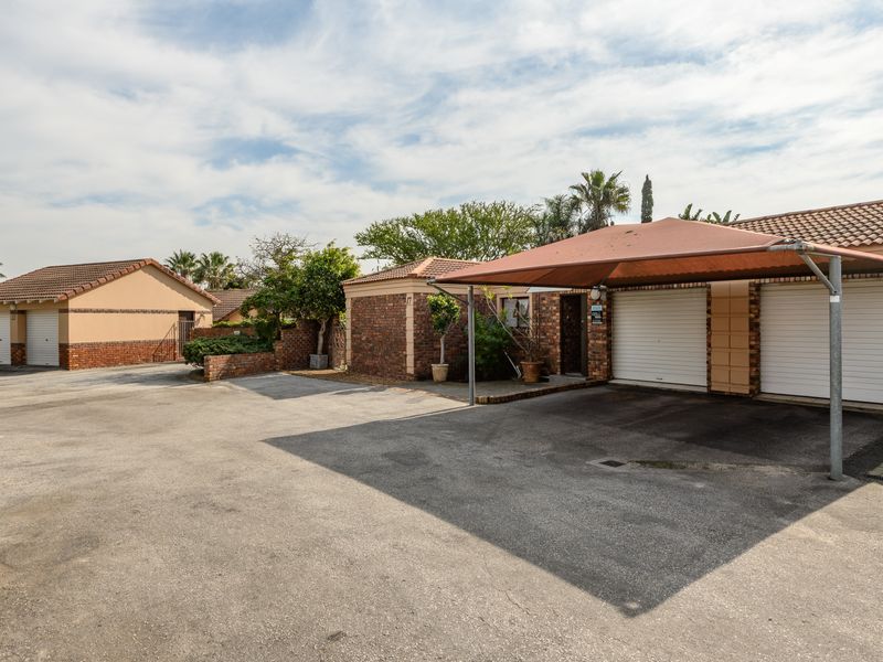 Exterior view of the townhouse featuring a paved driveway, double garage, and a shade cloth carport structure.