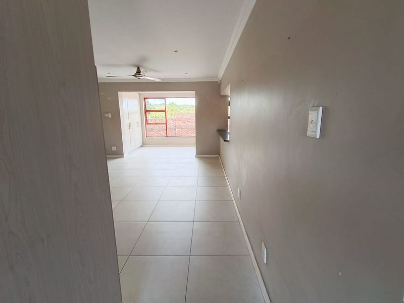 An empty open-plan living area featuring tiled flooring, a ceiling fan, built-in cupboards, and a breakfast bar counter.