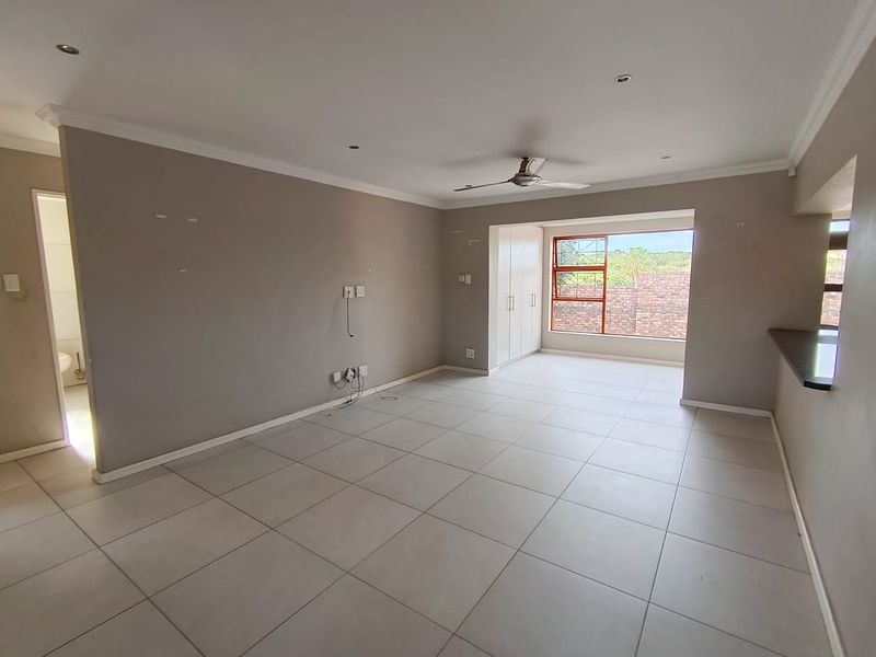 Spacious open-plan living area featuring neutral tiled flooring, a ceiling fan, built-in storage, and a breakfast bar overlooking the kitchen.