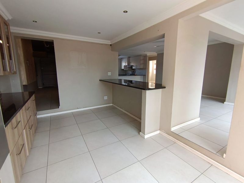Open plan kitchen and living area featuring tiled floors, granite breakfast bar, and neutral cabinetry in a clean, vacant space.