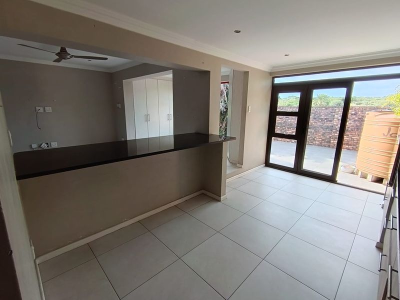 Spacious open-plan living area featuring tiled floors, a breakfast bar, built-in cupboards, and sliding glass doors leading to an outdoor patio area.