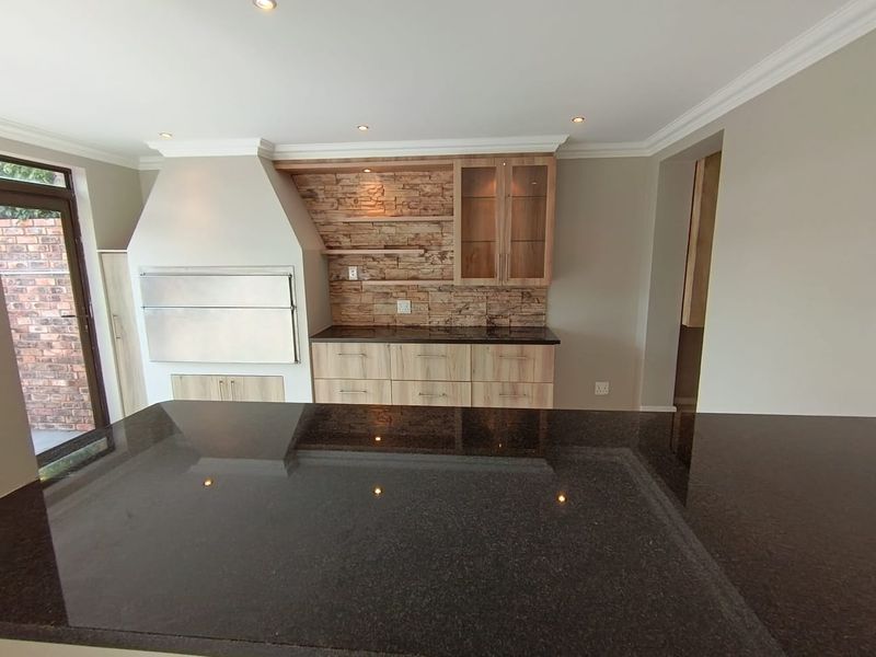 Modern open-plan living area featuring a built-in braai, stone cladding accent wall, granite countertops, and sleek wooden cabinetry with recessed lighting.