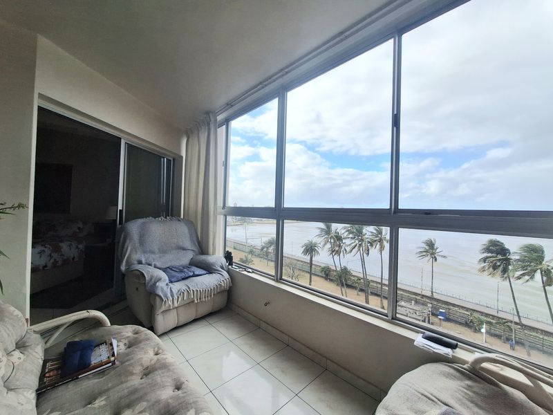 Enclosed balcony featuring large aluminium-framed windows with expansive coastal views and tiled flooring, providing a bright and versatile living space.