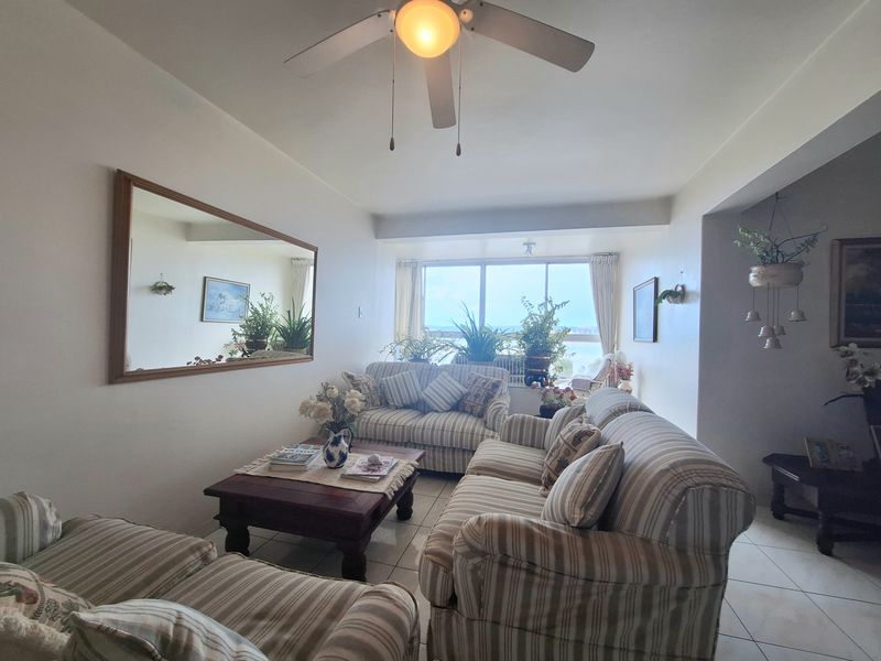 A comfortable living room featuring tiled flooring, a ceiling fan, and a large window providing natural light and exterior views.