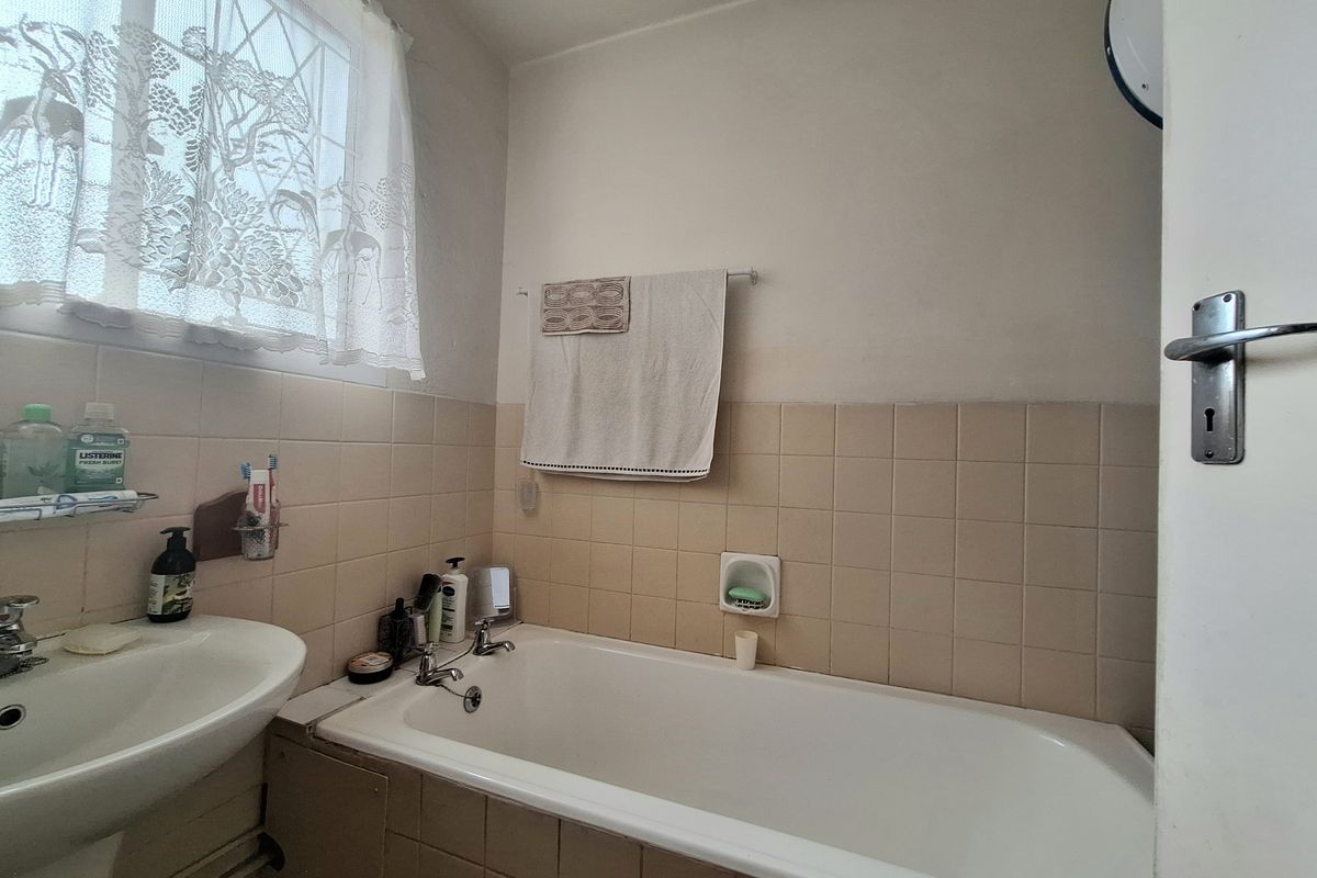A functional bathroom featuring a standard bathtub, pedestal basin, and neutral ceramic wall tiling.