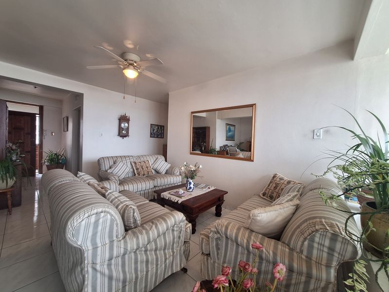 A comfortable living room featuring tiled flooring, a ceiling fan, and a wall-mounted mirror, providing a functional and well-lit space.