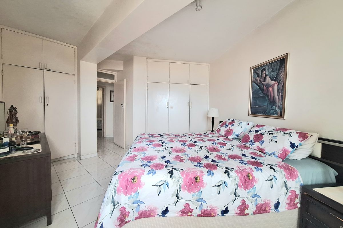 A spacious bedroom featuring extensive built-in cupboard storage and neutral tiled flooring, offering a functional layout with direct access to the hallway.