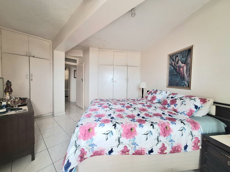 A spacious bedroom featuring extensive built-in cupboard storage and neutral tiled flooring, offering a functional layout with direct access to the hallway.