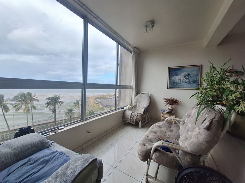Enclosed balcony featuring large windows with expansive coastal views, tiled flooring, and a bright, airy atmosphere suitable for a sunroom or relaxation area.