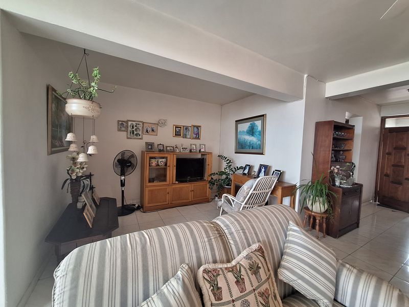 A spacious living area featuring neutral tiled flooring and an exposed structural beam, offering a functional layout for comfortable daily living.