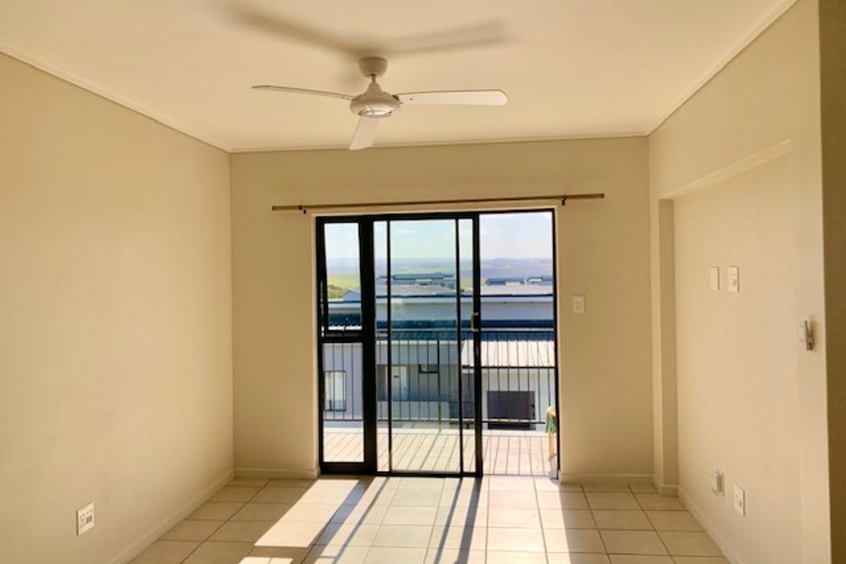 A bright, empty living room featuring tiled flooring, a ceiling fan, and a sliding glass door leading to a balcony with exterior views.