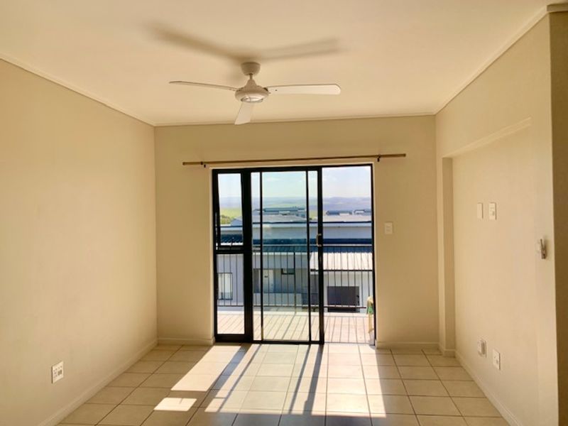 A bright, empty living room featuring tiled flooring, a ceiling fan, and a sliding glass door leading to a balcony with exterior views.