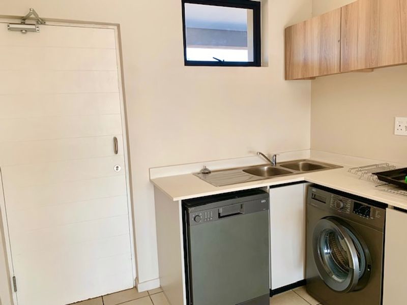 A functional laundry area featuring built-in cabinetry, a double sink, and space for under-counter appliances with tiled flooring.