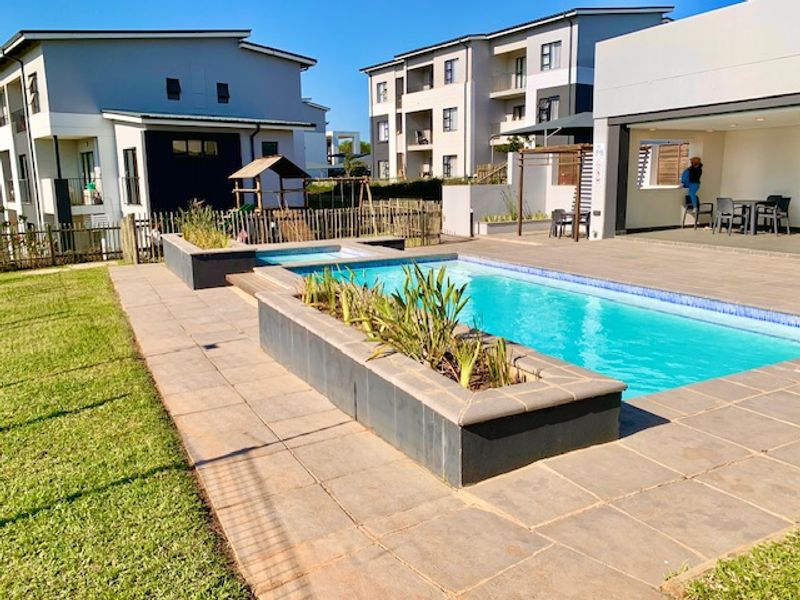Communal pool area featuring a tiled deck, raised planter beds, and an adjacent covered patio space within a modern apartment complex.