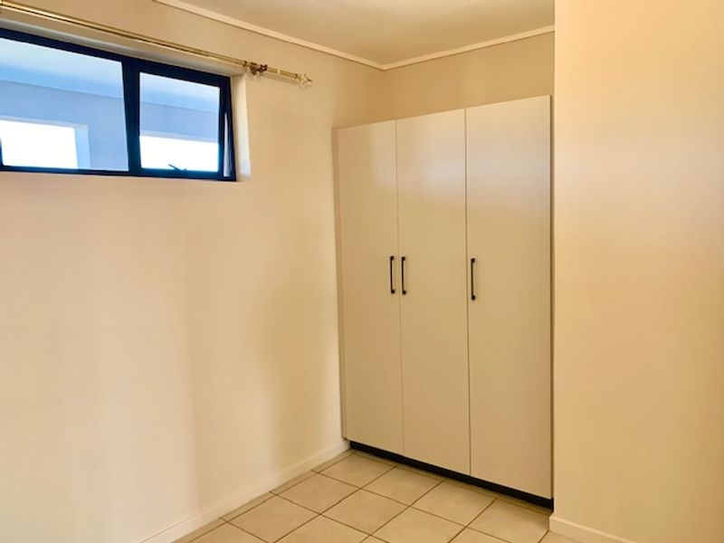 A clean, empty bedroom featuring neutral tiled flooring, a built-in wardrobe, and a top-hung window providing natural light.