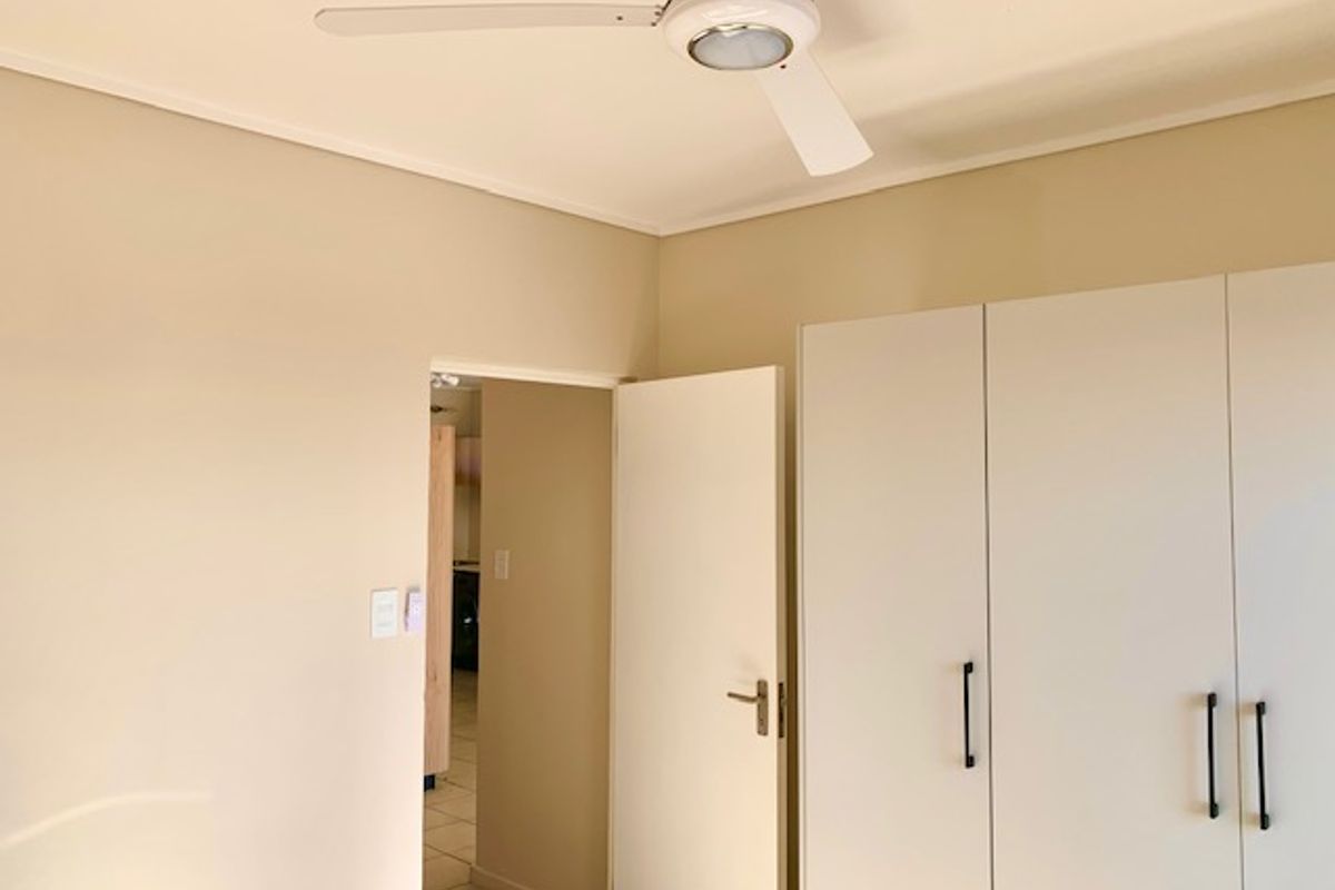 A clean, empty bedroom featuring built-in cupboards and a ceiling fan, offering a neutral canvas for personalization.