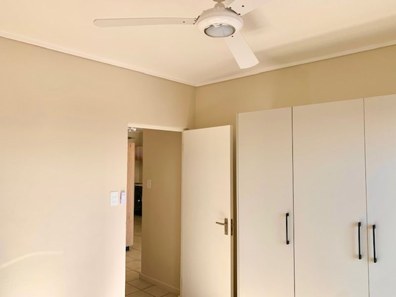 A clean, empty bedroom featuring built-in cupboards and a ceiling fan, offering a neutral canvas for personalization.