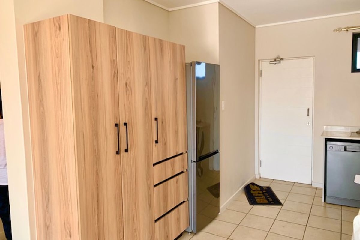 A functional kitchen area featuring light wood-toned built-in cabinetry, tiled flooring, and a clean, neutral layout with direct access to an exterior door.