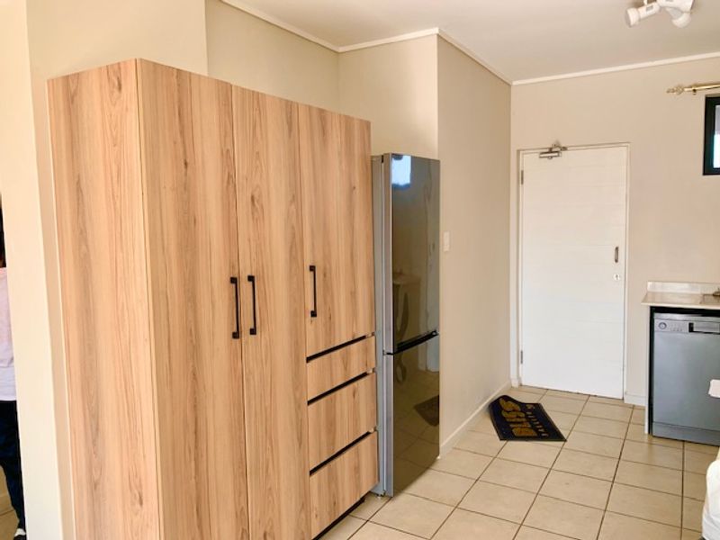 A functional kitchen area featuring light wood-toned built-in cabinetry, tiled flooring, and a clean, neutral layout with direct access to an exterior door.