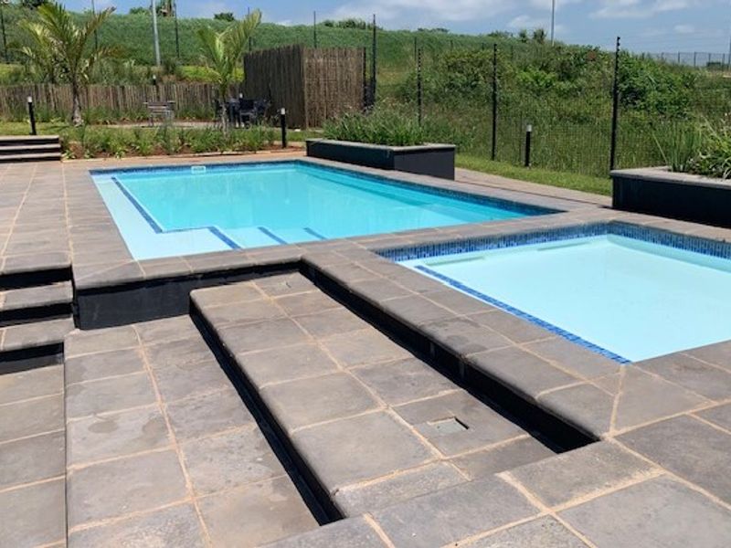 A well-maintained outdoor pool area featuring a swimming pool, a smaller splash pool, and paved decking with integrated planter boxes.