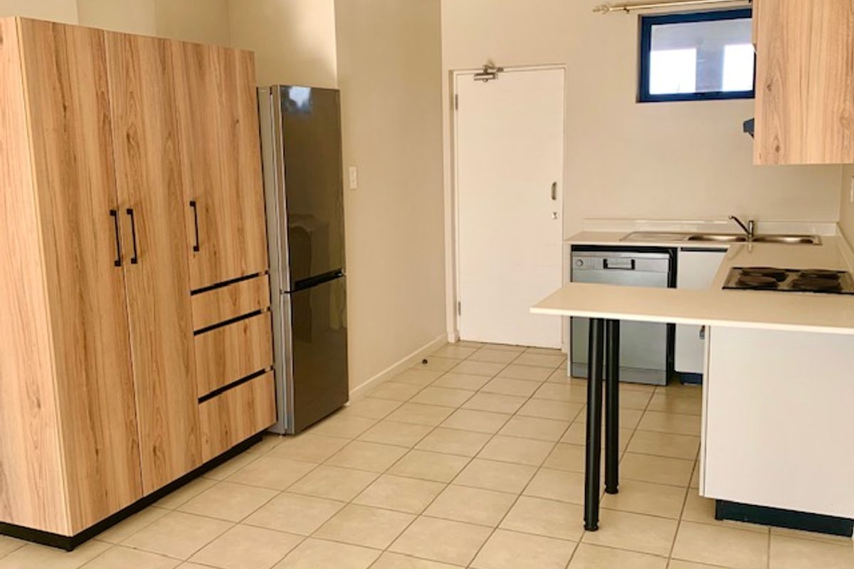 A functional kitchen featuring light wood-look cabinetry, a built-in hob, integrated dishwasher, and tiled flooring with a clean, neutral aesthetic.