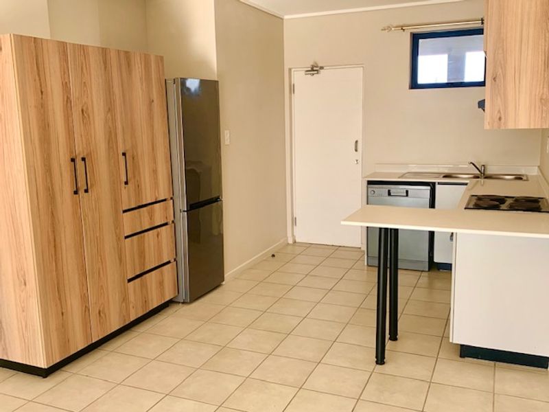 A functional kitchen featuring light wood-look cabinetry, a built-in hob, integrated dishwasher, and tiled flooring with a clean, neutral aesthetic.