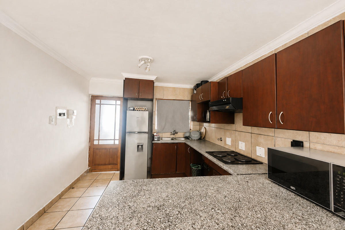 A functional kitchen featuring granite countertops, dark wood cabinetry, an electric hob with extractor fan, and direct access to an exterior door.