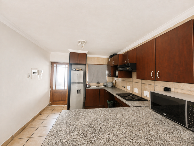 A functional kitchen featuring granite countertops, dark wood cabinetry, an electric hob with extractor fan, and direct access to an exterior door.