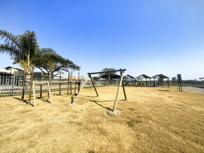 Outdoor communal area featuring a timber playground structure, dry lawn, and multiple covered picnic gazebos within a fenced estate setting.