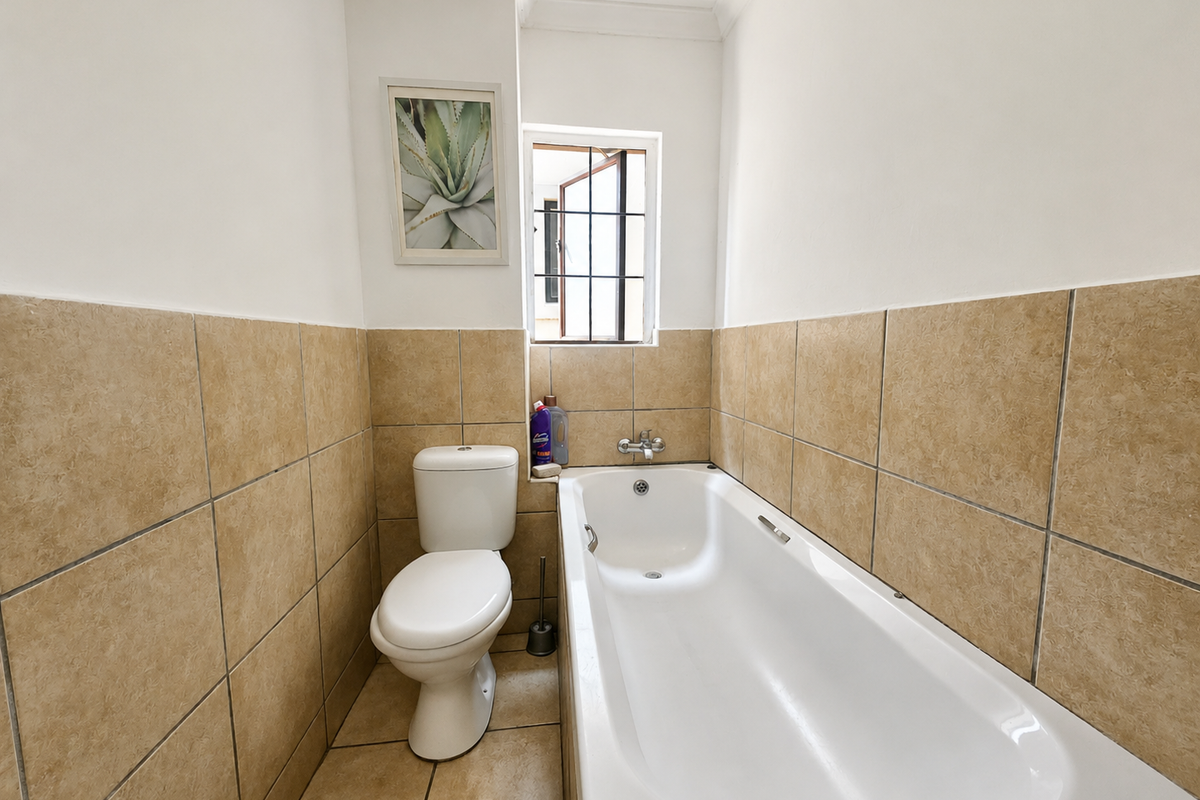 A functional bathroom featuring a standard bathtub, toilet, and neutral wall tiling with a small window for natural light.