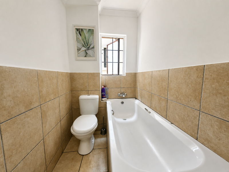 A functional bathroom featuring a standard bathtub, toilet, and neutral wall tiling with a small window for natural light.