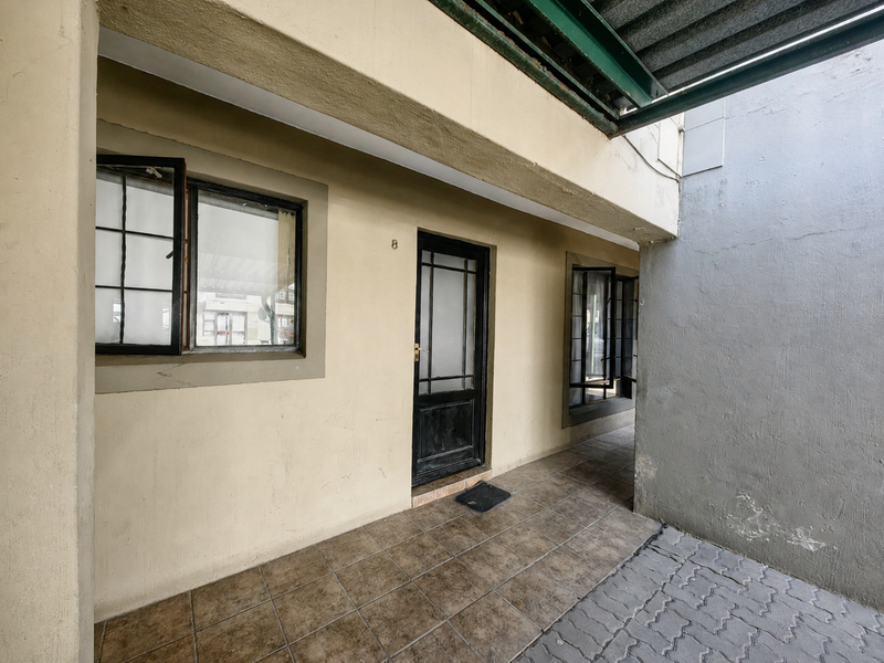 Exterior view of an apartment entrance featuring a covered walkway, tiled flooring, and security door access.
