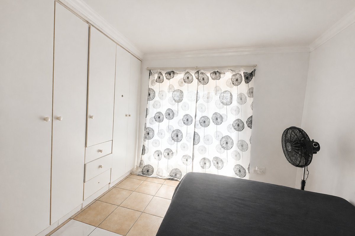 A bedroom featuring built-in cupboards, tiled flooring, and a curtained window, providing a functional space with potential for aesthetic updates.