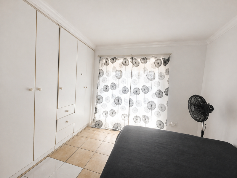 A bedroom featuring built-in cupboards, tiled flooring, and a curtained window, providing a functional space with potential for aesthetic updates.