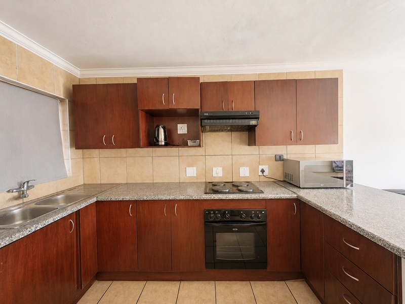A functional kitchen featuring dark wood cabinetry, granite countertops, a built-in oven, electric hob, and a double basin sink with tiled backsplash.