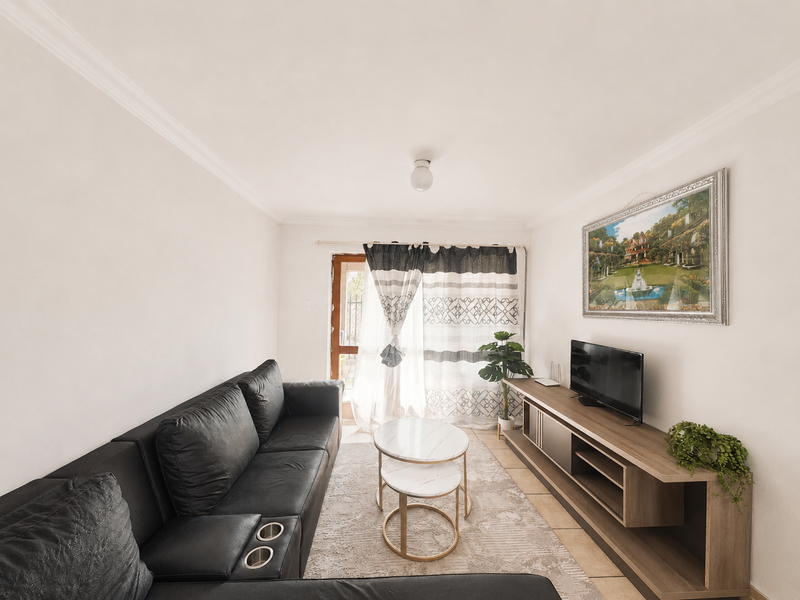 A well-maintained living room featuring neutral walls, crown molding, tiled flooring, and a glass sliding door providing natural light.