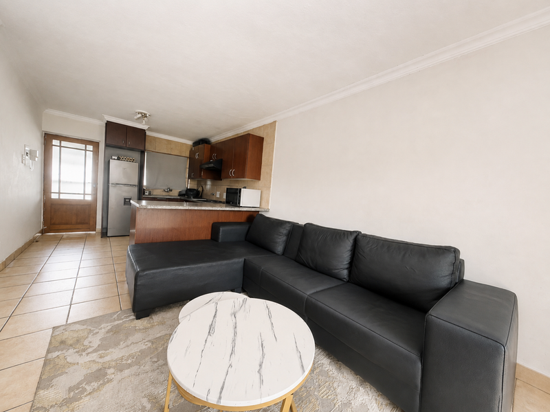 Open-plan living area featuring tiled floors, a compact kitchen with built-in cabinetry, and direct access to an exterior door.
